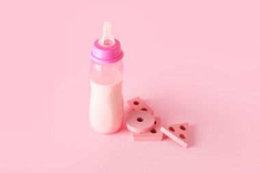 Pembe arka planda oyuncakları olan bebek için bir şişe süt.