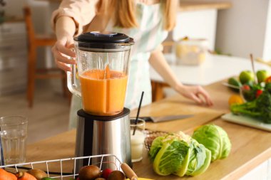 Genç bir kadın mutfakta blender ile sağlıklı smoothie yapıyor, yakın plan.