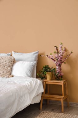 Yatağın yanındaki merdivende sakura dalları açan vazo.