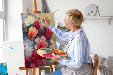 Mature female artist painting picture in  workshop clipart