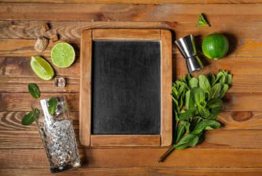 Buzlu bardak, ölçü kabı ve ahşap zemin üzerinde mojito hazırlamak için gerekli malzemeler.