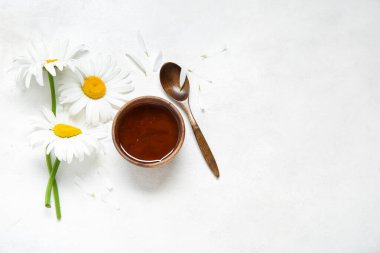 Bir kase bal, kaşık ve arka planda güzel papatya çiçekleri.