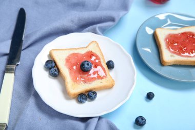 Renkli arkaplanda reçelli ve yaban mersinli tost tabakları, yakın plan.