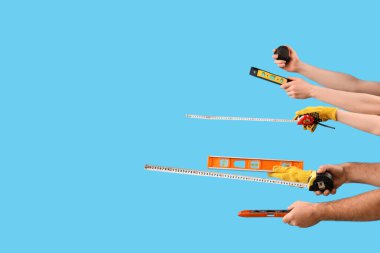 Kadın ve erkek el, mavi arka planda farklı bir inşaat aleti tutuyor.