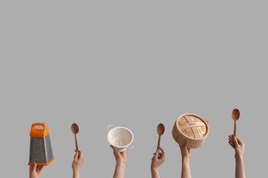 Gri arka planda farklı mutfak aletleri tutan kadın eller.