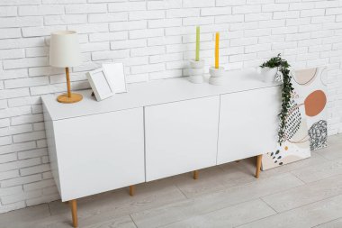 Lambalı beyaz çekmeceler, mumlar ve odandaki tuğla duvarın yanındaki boyalar.