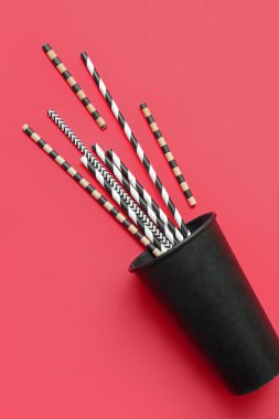 Kırmızı arka planda farklı içme pipetleri olan siyah kağıt bardak.