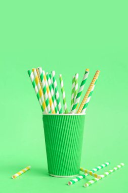 Yeşil arka planda farklı içme pipetleri olan kağıt bardak.