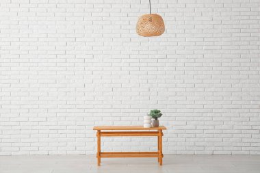 Tahta masa, bonsai ağacı ve beyaz tuğla duvarın yanındaki dekoratif figür.