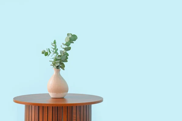 青い壁の近くの花瓶にユーカリの枝を持つ木製のコーヒーテーブル — ストック写真