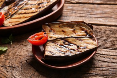 Lezzetli ızgara patlıcan ve ahşap arka planda domates tabağı.