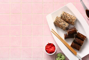 Lezzetli suşi ruloları, zencefil, wasabi ve pembe arkaplanda soya sosu.
