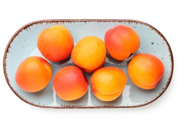 Beyaz arka planda izole edilmiş olgun kayısılarla dolu bir tabak.