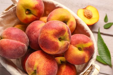 Tatlı şeftali ve beyaz ahşap arka planda yapraklarla dolu bir sepet.