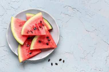 Tabakta taze karpuz parçaları ve mavi arka planda tohumlar var.