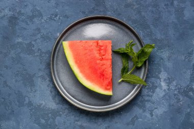 Mavi zemin üzerinde bir parça taze karpuz olan bir tabak.