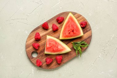 Taze karpuz parçaları ve gri arkaplanda ahududu olan tahta.