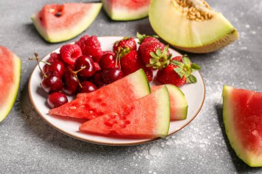 Taze karpuz parçaları ve gri arkaplanda farklı böğürtlenler.