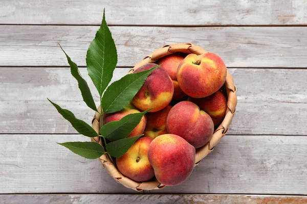 stock image Wicker bowl with sweet peaches and leaves on grey wooden background