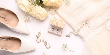 Alyansları, mücevherleri, kadın ayakkabıları, çiçekleri ve beyaz arka planda elbisesi olan bir kutu.