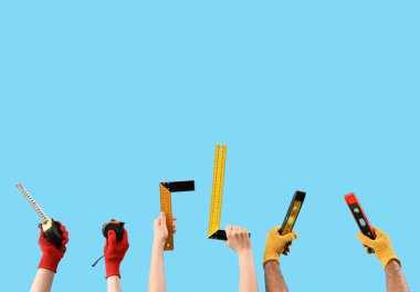 Kadın ve erkek el, mavi arka planda farklı bir inşaat aleti tutuyor.