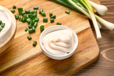 Ahşap arka planda dilimlenmiş yeşil soğanlı lezzetli ekşi krema kaseleri.