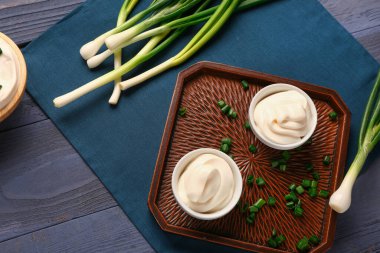 Lezzetli ekşi krema ve dilimlenmiş yeşil soğan, mavi ahşap arka planda.