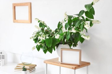 Üzerinde yasemin çiçekleri açan vazo ve oturma odasındaki raflarda boş çerçeve var.