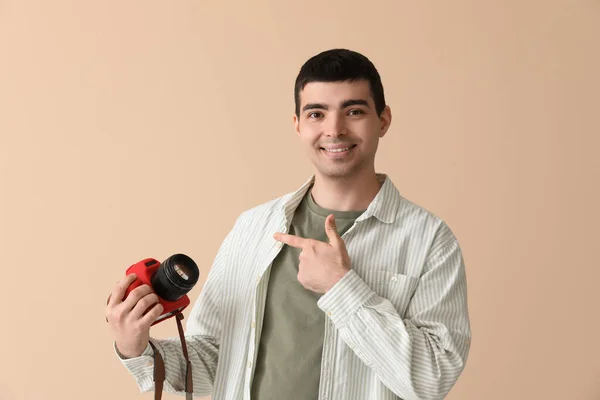 年轻的男性摄影师指着米色背景的专业相机 — 图库照片