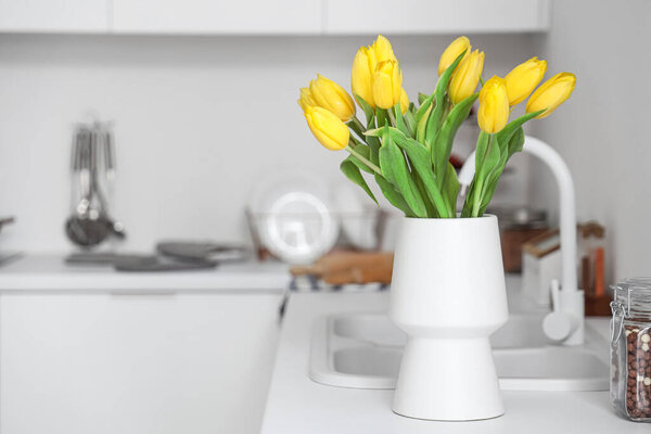 Vase with yellow tulip flowers on countertop near kitchen sink