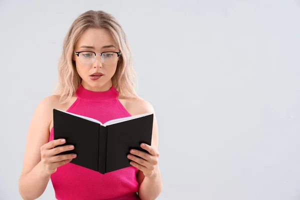 Shocked Young Woman Stylish Eyeglasses Reading Book Light Background — Stock Photo, Image