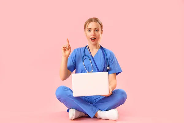 带笔记本电脑的女实习医生指着粉红背景的东西 — 图库照片
