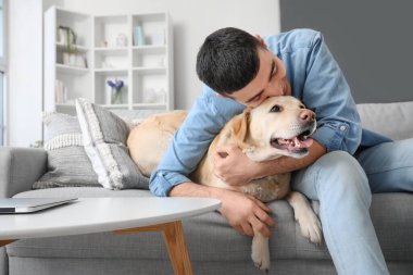 Labrador köpeği olan genç adam evdeki kanepede oturuyor.