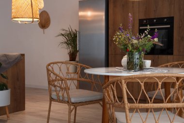 Modern mutfağın içinde, yemek masasında parlayan lamba ve vazo var.