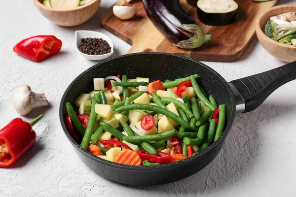 stock image Frying pan with fresh vegetables on light background