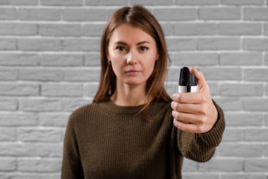 Young woman with pepper spray for self-defence on grey brick background, closeup