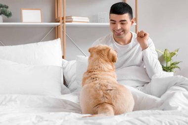 Labrador köpeği olan genç adam yatak odasında oturuyor.