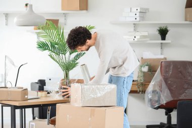 Genç adam ofisinde streç filmle çiçek paketliyor.