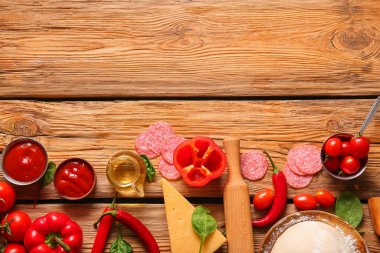Tahta arka planda pizza hazırlamak için farklı malzemeler.