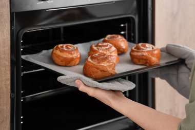 Kadın elektrikli fırından taze tarçınlı tepsi alıyor.