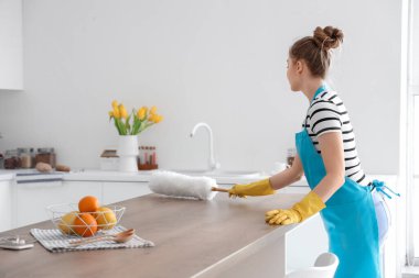 Güzel genç bir kadın yemek masasını temizliyor. Mutfakta toz fırçasıyla.
