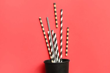 Kırmızı arka planda farklı içme pipetleri olan siyah kağıt bardak.