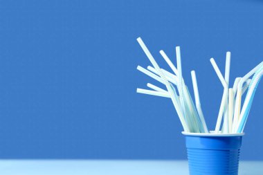 Mavi arka planda farklı içme pipetleri olan plastik bardak.