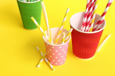 Sarı arka planda farklı pipetli kağıt bardaklar.