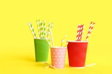 Sarı arka planda farklı pipetli kağıt bardaklar.