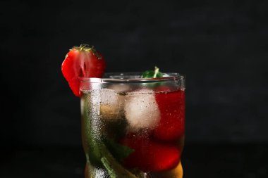 Bir bardak buzlu çay, çilekli ve siyah arkaplanda nane.