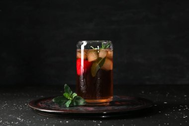 Bir bardak buzlu çay, çilekli ve siyah arkaplanda nane.