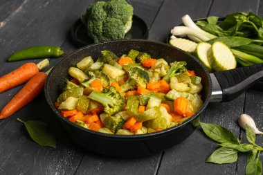 Koyu ahşap arka planda farklı sebzelerle kızartma tavası