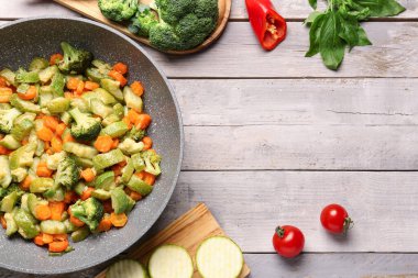 Gri ahşap arka planda farklı sebzelerle kızartma tavası.