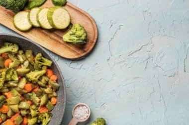 Tahta ve tavada gri arka planda farklı sebzeler var.